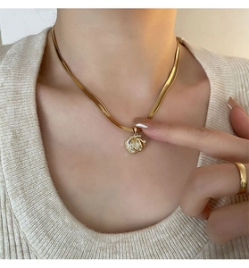 Detail of gold snake chain necklace with shell pendant and pearl inlay on model neck