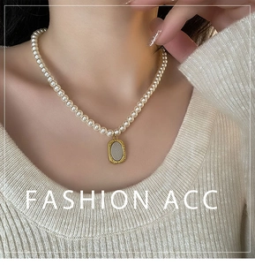 Détail du collier de perles avec pendentif rose porté sur un pull en maille beige