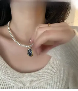 Détail d'un collier de perles avec pendentif camée rose bleue sur un pull en maille