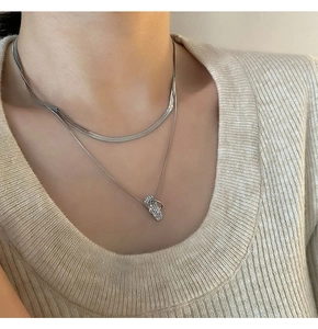 Detail of layered silver necklaces with a mini flip-flop pendant and snake chain
