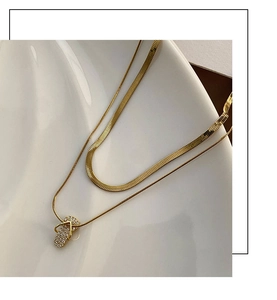 Close-up of double layer gold flip-flop pendant necklace with herringbone chain on a tray