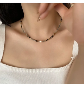 Detailed close-up of beaded choker with baroque pearl and tiger eye stones on neck
