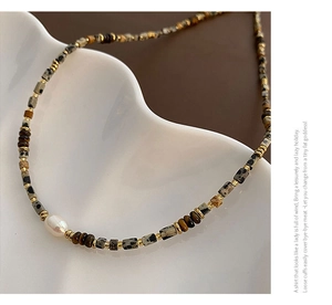 Detailed close-up of Baroque pearl and Tiger eye stone beads on a white ceramic plate