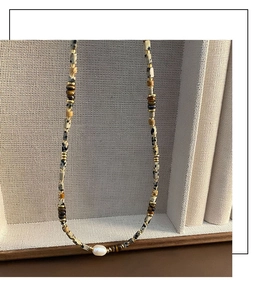 Detailed shot of baroque pearl and tiger eye beaded necklace on a textured stand