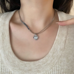 Double-layered silver necklace with shell pendant and stones on a beige sweater
