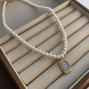 Élégant collier de perles avec pendentif rose dorée sur un écrin à bijoux en velours beige
