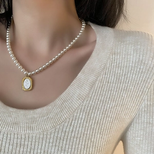 Collier de perles élégant avec pendentif rose dorée rétro porté sur un pull beige