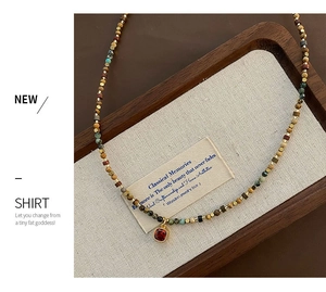 Macro detail of natural stone beaded necklace with a red gemstone pendant on linen tray