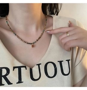 Detail of beaded necklace with orange zircon pendant on model wearing beige shirt