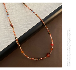 Close-up of red agate and Czech beads necklace with golden spacers on a textured surface