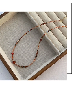 Close-up of handmade red agate beaded necklace on a wooden jewelry tray with golden clasp