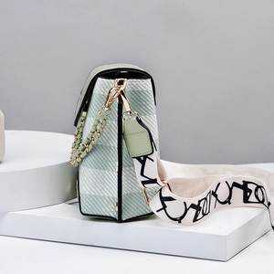 Chic light green checkered crossbody bag with stylish wide logo strap on white pedestal