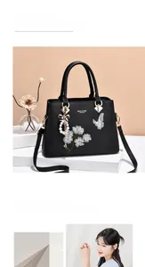 Detail einer eleganten schwarzen Handtasche mit weißer Blumenstickerei und Perlenquaste