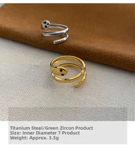 Detail of snake wrap rings in gold and silver finish with green zircon eyes