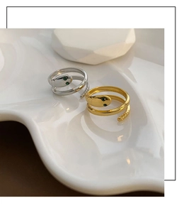 Detail view of gold and silver snake rings with green gemstone eyes on a ceramic tray