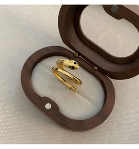 Macro detail of gold snake ring with green gem eyes in an elegant wooden jewelry box