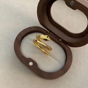 Golden stainless steel snake ring with green eye detail displayed in a wooden jewelry box