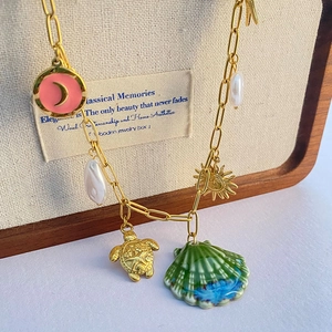 Bohemian gold chain necklace featuring sea shell, turtle, and moon charms on wood stand