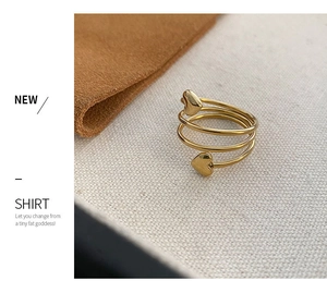Detail of a gold multilayer heart ring on warm textured fabric with minimalist aesthetics