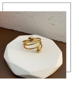 Detail of a golden multi-layer spiral ring featuring two polished heart charms on a tray
