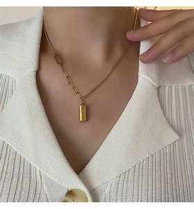 Gros plan du collier asymétrique avec pendentif lingot d'or sur un gilet en tricot