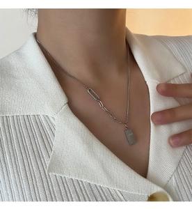 Détail du collier pendentif barre argentée avec chaîne asymétrique sur un pull blanc