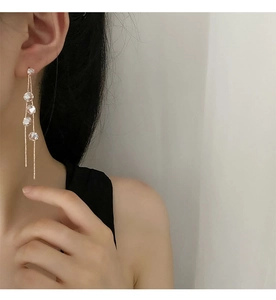 Close-up of long tassel earrings with sparkling crystals on female model in light gold