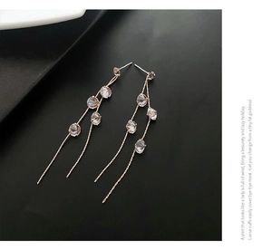 Close-up of long rose gold tassel earrings with zircon crystals on a black background