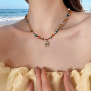 Collana con pendente a sole bohémien e perline in pietra naturale su sfondo spiaggia vacanza