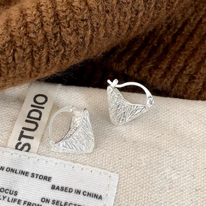 Macro shot of silver triangular earrings with intricate woven texture and hoop clasp