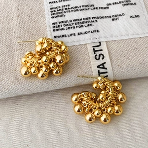 Modern C-shaped cluster stud earrings with gold-plated metallic spheres on canvas