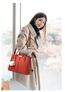 Detail of red textured leather handbag with pearl and fur ball charm on beige coat