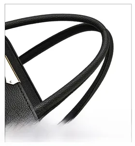 Detail of black pebble leather handbag featuring thick cylindrical handles and gold hardware