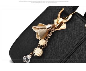 Detail of black lychee grain leather handbag featuring golden floral and pearl charm