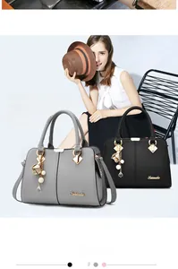 Detail of lychee pattern leather tote with golden logo and elegant pearl pendant
