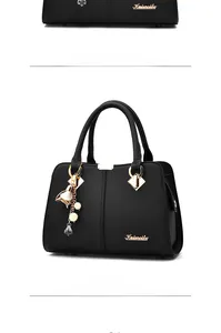 Detail of black pebbled leather handbag with gold hardware and floral pearl pendant