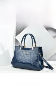 Detail of navy blue glossy crocodile pattern leather handbag with gold metal logo