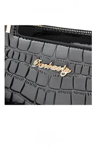 Detail of black patent leather bag with crocodile pattern and gold Danbaoly logo