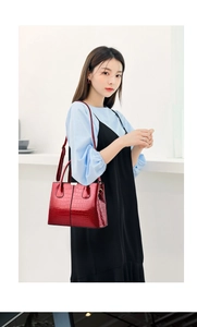 Detailed view of red crocodile-pattern leather handbag with gold hardware and shoulder strap