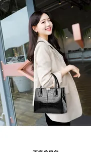 Detail of black glossy crocodile pattern tote bag carried by a model in a beige suit