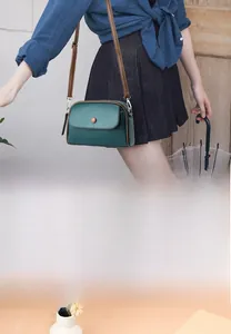 Detail of a mini dark green litchi grain leather crossbody bag with brown strap
