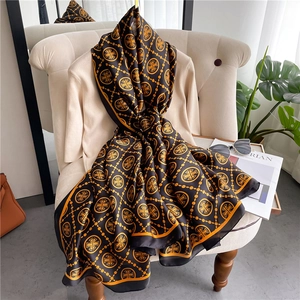Luxurious long silk scarf with orange chain patterns draped over a chair and sweater