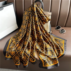 Close-up of luxury silk scarf with gold medallion pattern draped on a leather bag