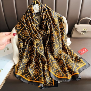 Detail of luxury silk scarf with gold chain print and orange edges on a black background