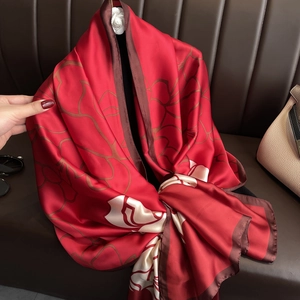 Detailed close-up of a large red luxury silk scarf with abstract floral patterns and brown trim