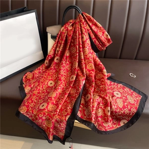 Luxurious red silk scarf with gold floral patterns draped over a stylish handbag