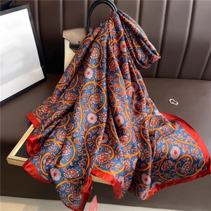 Detailed close-up of luxury silk-feel scarf featuring orange floral patterns and red borders