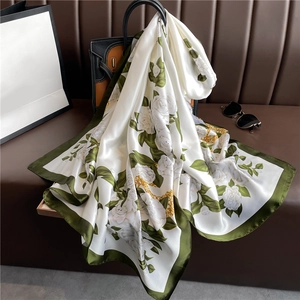 Detail eines luxuriösen Seidenschals mit weißen Rosen und olivgrünem Rand auf einer Tasche