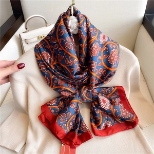 Close-up of silk scarf with orange chain pattern and red border on beige sweater