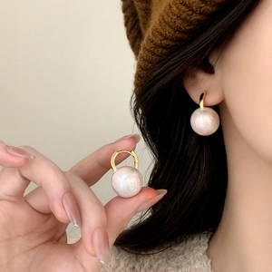 Elegant gold drop earrings with pearl white resin beads worn by a model in fall style